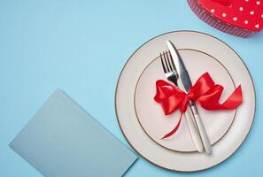 Round plate and tied fork with knife on blue background, festive table setting photo