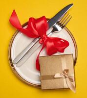Round plate and tied fork with knife on yellow background, festive table setting photo