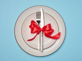 Round white plate and tied with red bow view with knife on yellow background, festive table setting photo