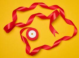 Spool of red silk ribbon on yellow background, top view photo