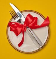 Round white plate and tied with red bow view with knife on yellow background, festive table setting photo