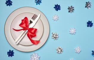 Round white plate and tied with red bow view with knife on a blue background, festive table setting photo