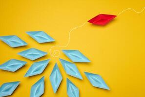Group of blue paper boats heading in one direction and one red one heading in the opposite direction. Concept of individuality, uniqueness and talent of the employee. photo