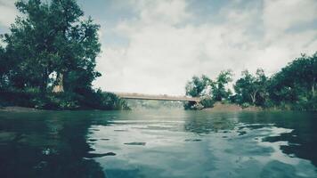 Tranquil riverside view with bridge and lush greenery under cloudy sky video