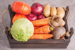 Vegetables in a wooden box on a concrete background. Cabbage, carrots, onions, pumpkins and beets. photo