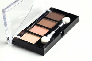 A palette of beige, brown warm eyeshadow with an applicator on a white background photo