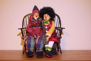 Two sad looking clowns together on a bench, painted faces with red clown noses. photo