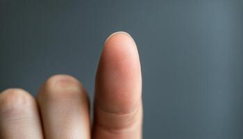 A human finger is directed upwards against a muted background, showcasing skin texture photo
