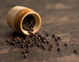 Close up of black pepper or peppercorns with a clay pot on a stone background. photo