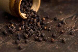 Close up of black pepper or peppercorns with a clay pot on a stone background. photo