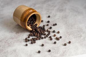 Close up of black pepper or peppercorns with a clay pot on a stone background. photo