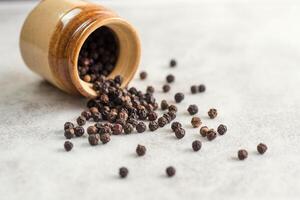 Close up of black pepper or peppercorns with a clay pot on a stone background. photo
