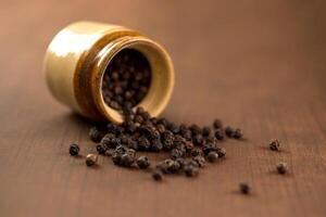 Close up of black pepper or peppercorns with clay pot on a wooden background. photo