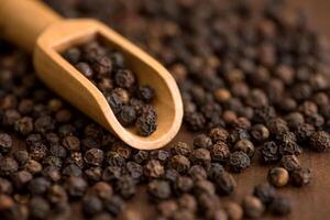 Close up of black pepper or peppercorns in wood scoop on a wooden background. photo