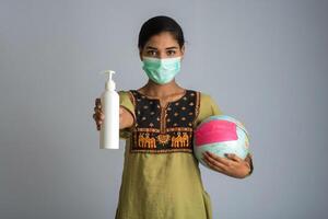 Portrait of young girl using or showing a sanitizing gel from a bottle for hands cleaning and holding world globe with mask. photo