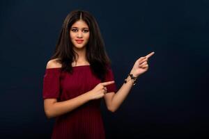 Portrait of a successful cheerful young girl pointing and presenting something with hand or finger with a happy smiling face. photo