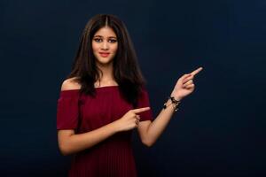 Portrait of a successful cheerful young girl pointing and presenting something with hand or finger with a happy smiling face. photo
