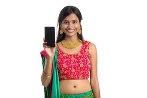 Young Indian traditional girl using a mobile phone or smartphone and showing blank screen smart phone on white background photo