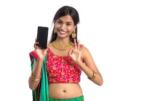Young Indian traditional girl using a mobile phone or smartphone and showing blank screen smart phone on white background photo