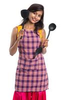 Joven india sosteniendo una cuchara de utensilios de cocina, stapula, cucharón y sartén, etc. sobre un fondo blanco. foto