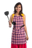 Joven india sosteniendo una cuchara de utensilios de cocina, stapula, cucharón y sartén, etc. sobre un fondo blanco. foto