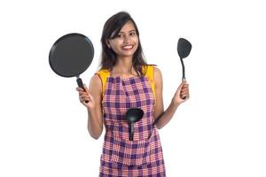 Joven india sosteniendo una cuchara de utensilios de cocina, stapula, cucharón y sartén, etc. sobre un fondo blanco. foto