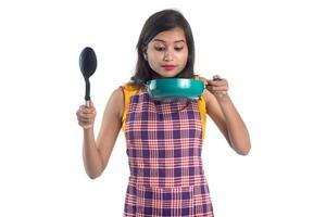 Joven india sosteniendo una cuchara de utensilios de cocina, stapula, cucharón y sartén, etc. sobre un fondo blanco. foto