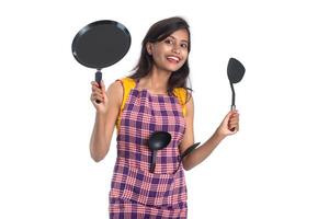 Joven india sosteniendo una cuchara de utensilios de cocina, stapula, cucharón y sartén, etc. sobre un fondo blanco. foto