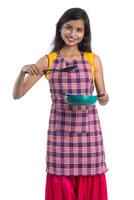 Joven india sosteniendo una cuchara de utensilios de cocina, stapula, cucharón y sartén, etc. sobre un fondo blanco. foto