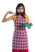 Joven india sosteniendo una cuchara de utensilios de cocina, stapula, cucharón y sartén, etc. sobre un fondo blanco. foto