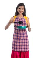 Joven india sosteniendo una cuchara de utensilios de cocina, stapula, cucharón y sartén, etc. sobre un fondo blanco. foto