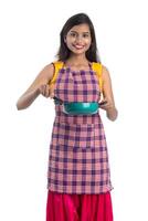 Joven india sosteniendo una cuchara de utensilios de cocina, stapula, cucharón y sartén, etc. sobre un fondo blanco. foto