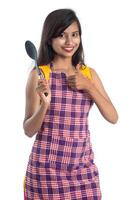 Joven india sosteniendo una cuchara de utensilios de cocina, stapula, cucharón y sartén, etc. sobre un fondo blanco. foto