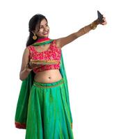 Beautiful young happy girl taking a selfie with clay lamp or diya during the festival of light Diwali using a smartphone on a white background photo