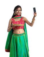 Beautiful young happy girl taking a selfie with clay lamp or diya during the festival of light Diwali using a smartphone on a white background photo
