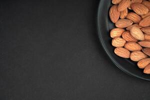 Almonds in black plate and Black Background, corner view, flat lay photo