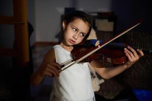 Young girl practicing violin with focused expression indoors photo