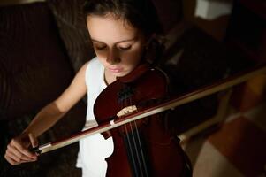 Young girl practicing the violin with concentration indoors photo