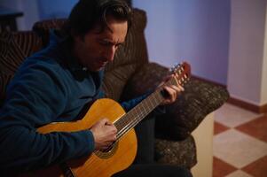 Man playing acoustic guitar on sofa in cozy room with warm lighting highlighting his musical focus photo