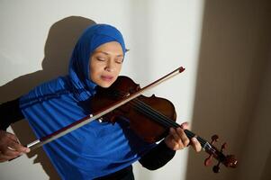 Woman in blue headscarf playing violin with closed eyes photo