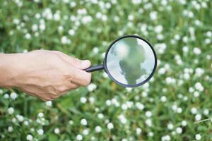 Close up hand hold magnifying glass to inspect tiny things in nature. Concept, exploring, searching, analysis. Study survey and research about ecology environment. photo