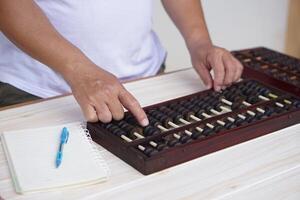 Close up man hand calculate and count wooden abacus. Concept, ancient style calculation. Counting equipment. Calculator. Educational material. Math teaching aid photo