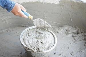 Close up worker hand hold a trowel to mix wet cement in bucket. Concept. Construction job. Process of construction work with cement. Choose good quality and proper material product for building photo