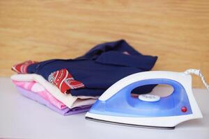 Electric iron and stack of folded clothes on table. Concept, daily chore, household. ironing and folded clothes for neat and clean. Maintenance and keep garments. photo