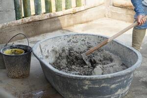 Close up worker using a hoe to mix cement powder, sand, stones in basin for mixing cement. Concept. Construction worker job. Hard working. Process of construction work with cement photo