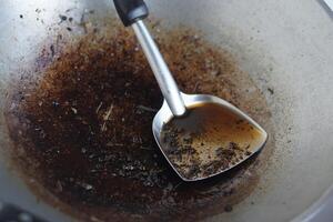 Close up cooked oil in a ladle with burnt stain of fried food scrape in pan. Concept, unhealthy cooking. Oil used for frying food should not be reused because it contains carcinogens. Health care. photo