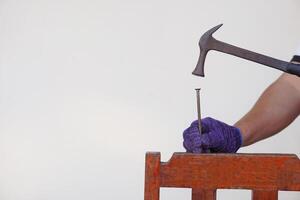 Closeup carpenter hand uses hammer to hit nail. Concept, carpentry and construction tools. Repair or fixing, DIY woodwork. photo