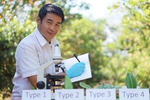 Handsome Asian man is doing science experiment by using microscope, inspect, analysis and research. Concept, science subject, project work. Experiment, education. Outdoor class. photo