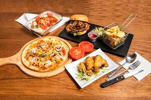 Black Truffle Mushroom and Shrimp Pizza, Lemon honey chicken wings, Spanish baked Pork Chop Rice and Italian Mushroom Beef Cheese Burger on table with fork, knife and spoon side view of italian food photo
