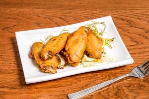 Lemon honey chicken wings with cabbage served in tray dish with fork isolated on wooden table side view of fast food photo